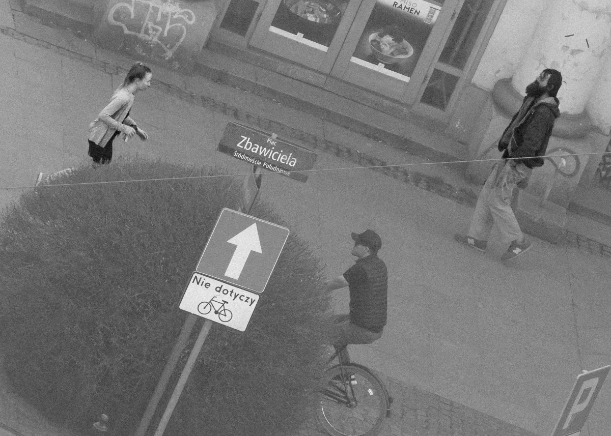 Overhead black-and-white street scene with a cyclist, pedestrians, and a Zbawiciela sign